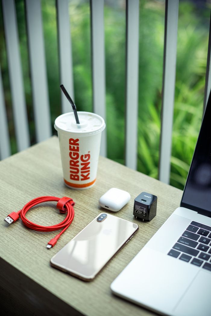 From above of laptop with mobile phone and disposable cup of fresh beverage placed on wooden surface